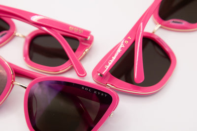 Close-up of cat eye sunglasses showing vibrant pink acetate frames, gold Sol Kyst branding, and dark nylon lenses.